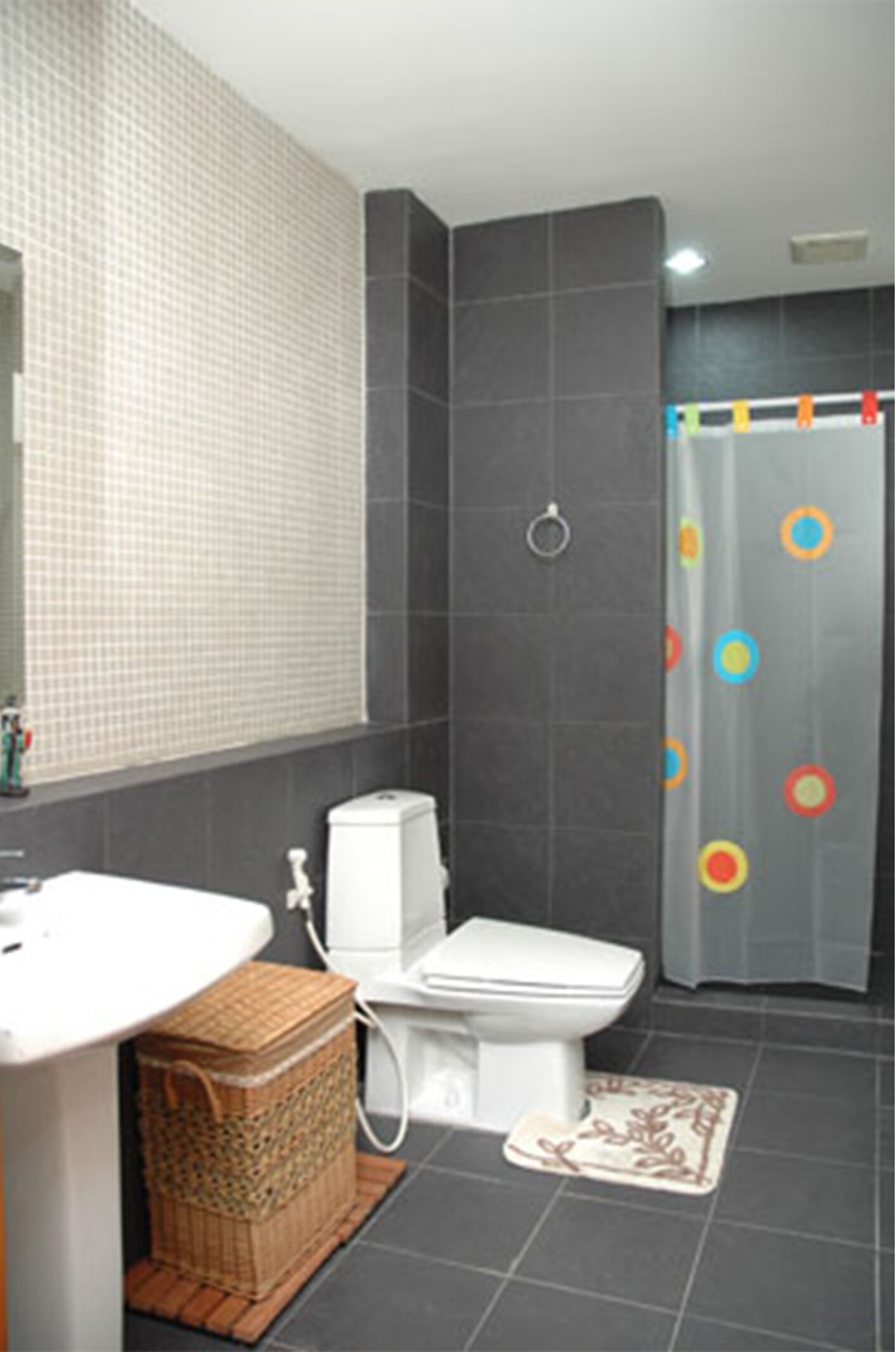Un baño con lavamanos blanco, inodoro, cesta de mimbre y cortina de ducha con círculos de colores.