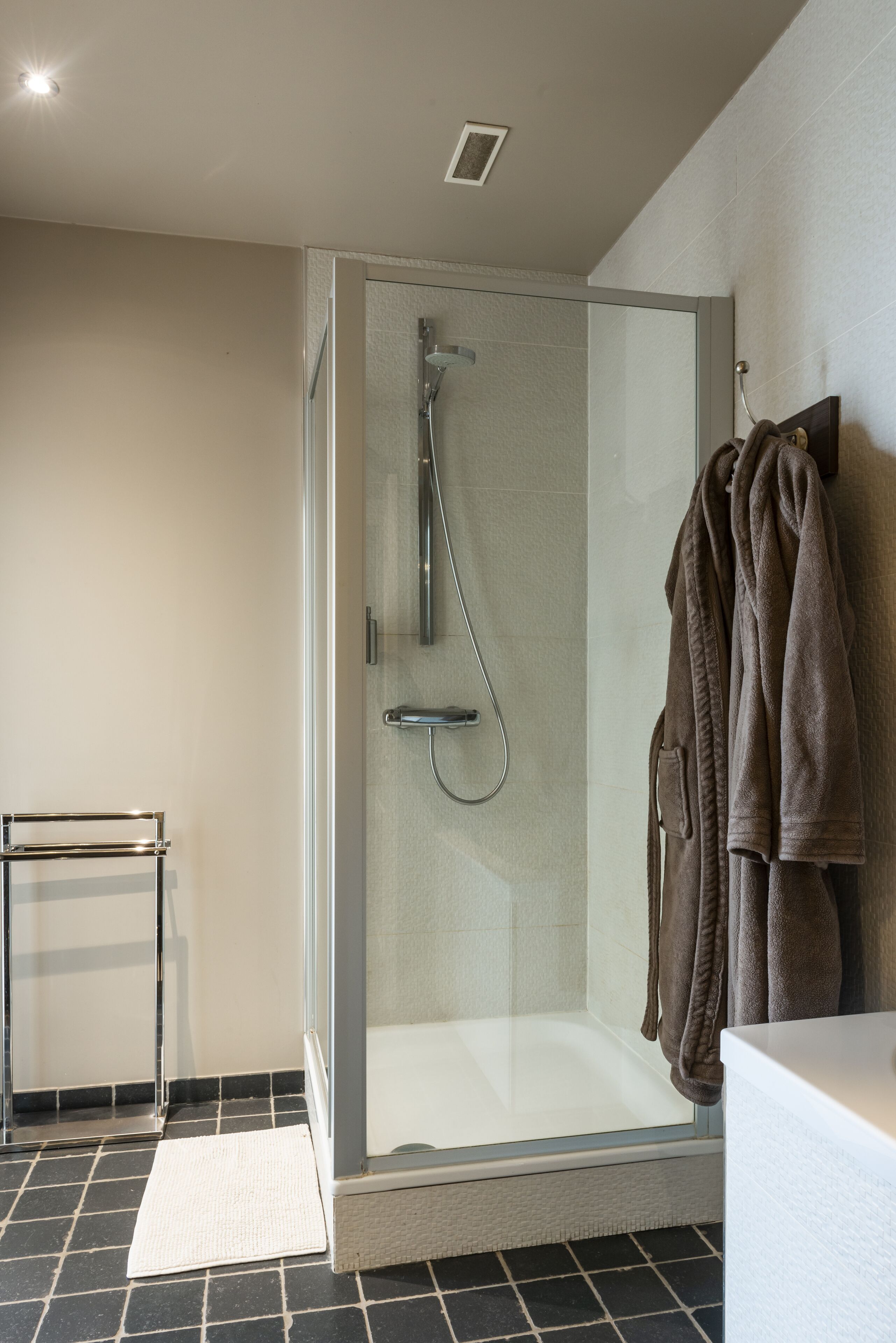 A modern bathroom with a glass-enclosed shower, a white bathtub, and a towel rack with multiple towels.