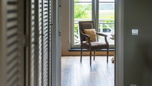 A room with a wooden floor, a chair with a cushion, and a sliding glass door leading to an outdoor area. - La Cereza (Oudenaarde)