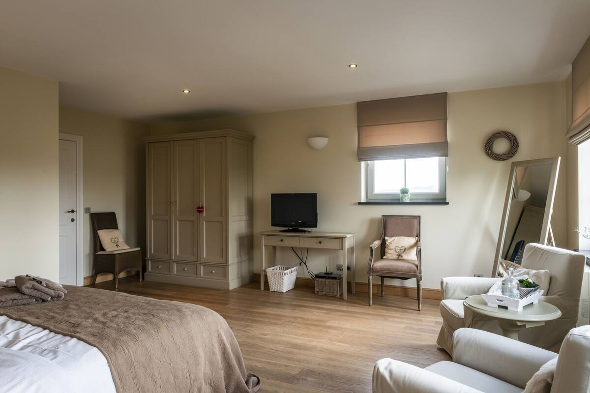 A bedroom with a bed, a desk with a television, a chair, a wardrobe, and a window with blinds.