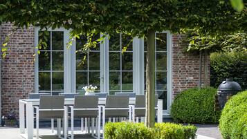 A patio with outdoor seating, a brick building, and a well-maintained hedge.