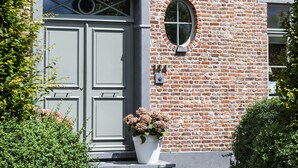 A brick building with a double door and a small window. There is a potted plant in front of the door. - La Cereza (Oudenaarde)