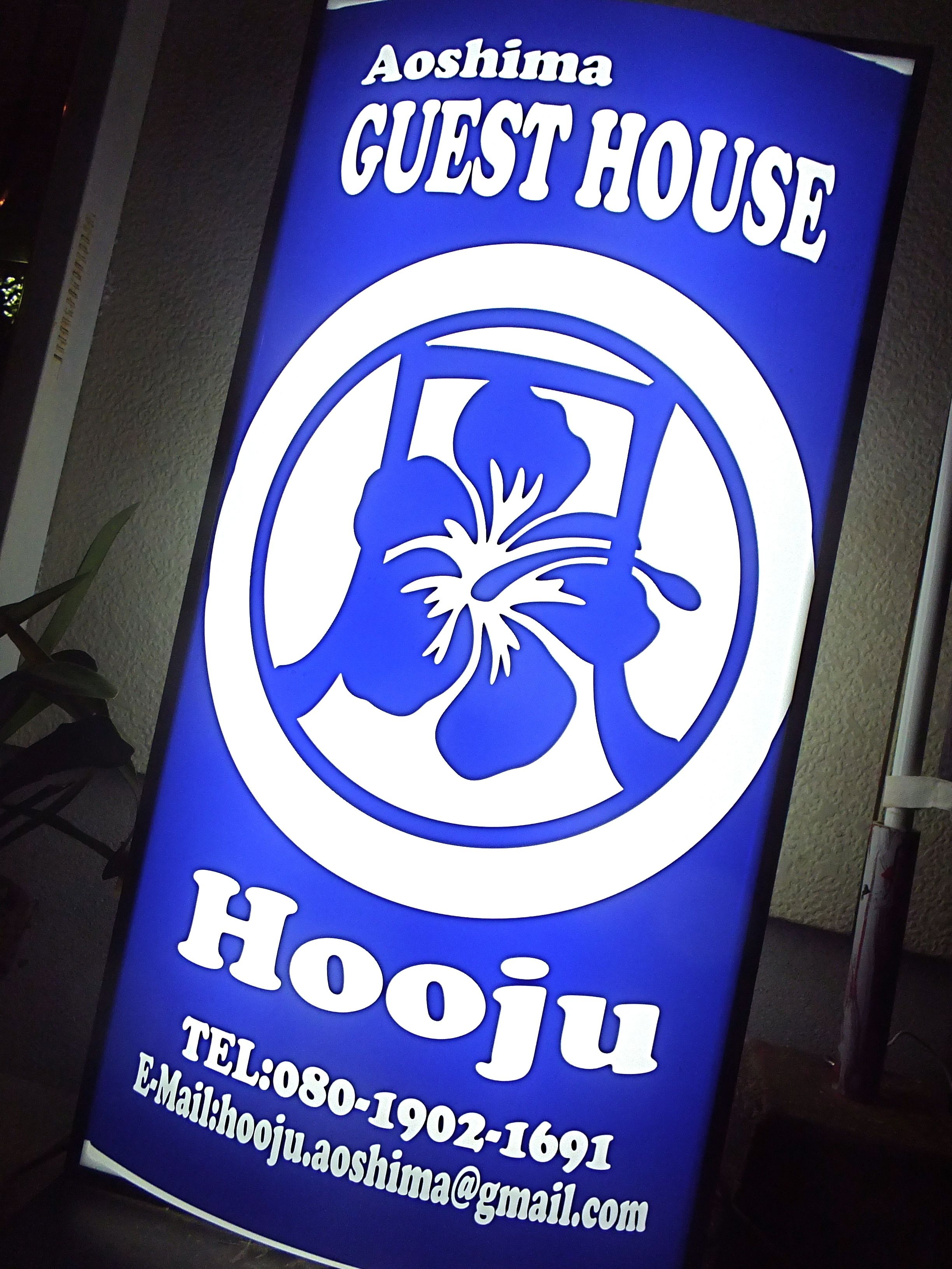 Un letrero azul con texto blanco para Aoshima Guest House, que incluye información de contacto.