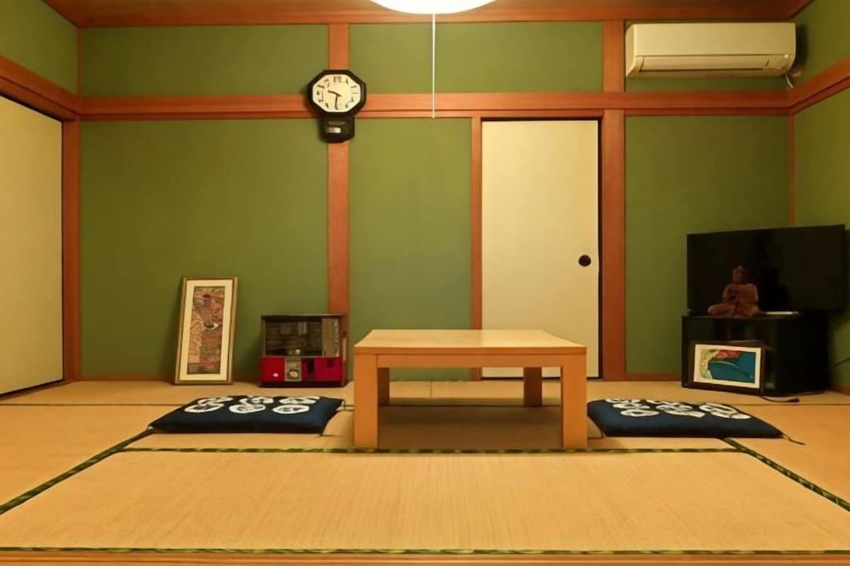 A tatami mat room with a wooden table, a clock, a TV, and a small statue.