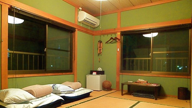 A room with tatami mats, two beds, a heater, and a small table with items on it. - Aoshima Guesthouse Hooju - Hostel (Miyazaki)