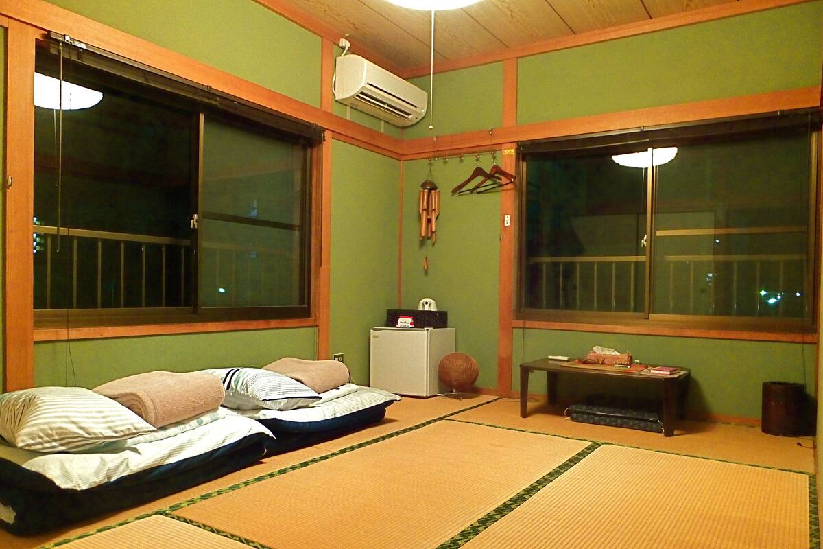 Een kamer met tatami matten, twee bedden, een verwarming en een kleine tafel met spullen erop.
