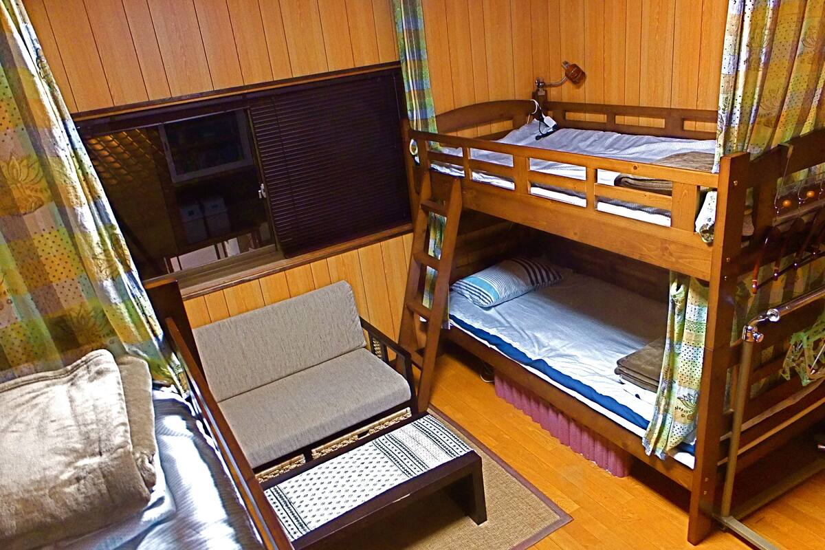 Een stapelbed met een televisie op het bovenbed, een klein tafeltje en een bank.