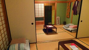 A traditional Japanese room with tatami flooring, a low table, a bed with pillows, and a sliding door. - Aoshima Guesthouse Hooju - Hostel (Miyazaki)