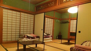 A traditional Japanese room with tatami flooring, a low table, and a bed with pillows. - Aoshima Guesthouse Hooju - Hostel (Miyazaki)