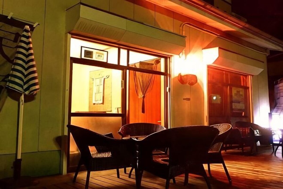 L’extérieur d’un hôtel de nuit, avec une terrasse en bois, des sièges en plein air et une entrée illuminée.