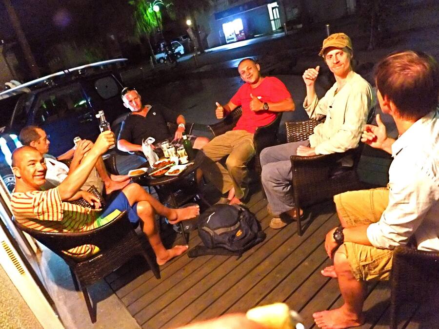 A group of people seated around a table on a wooden deck, engaged in conversation.