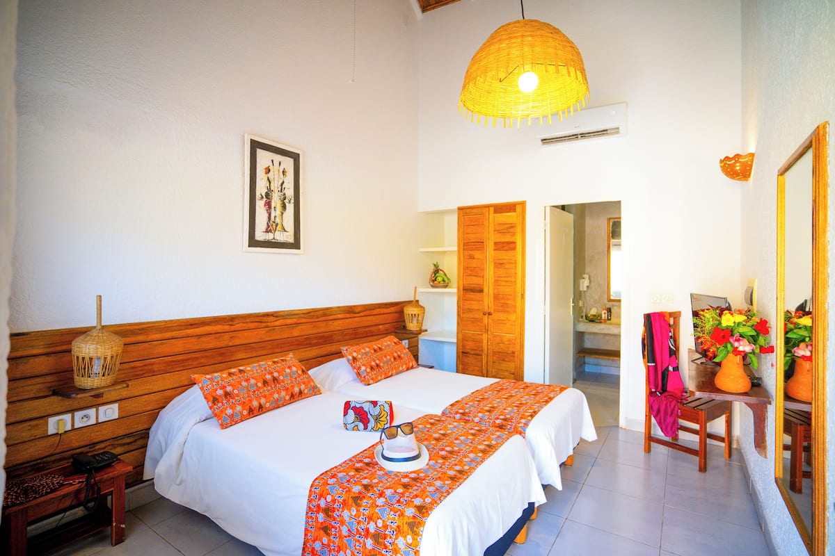 A bedroom with a wooden headboard, a bed with white bedding and orange accents, a bedside table with a lamp, and a mirror on the wall.