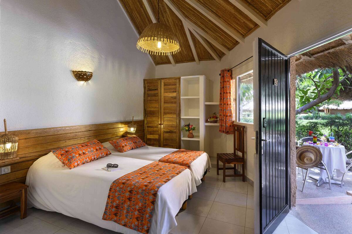 A hotel room with two beds, a wooden ceiling, a large window, and a view of the outdoors.