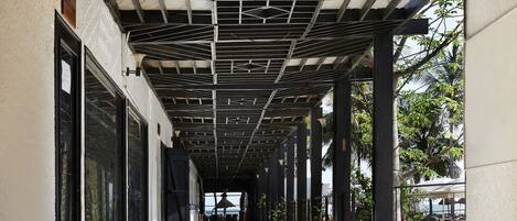 Un pasillo cubierto con estructura de techo metálico, ventanas grandes y una planta en maceta.