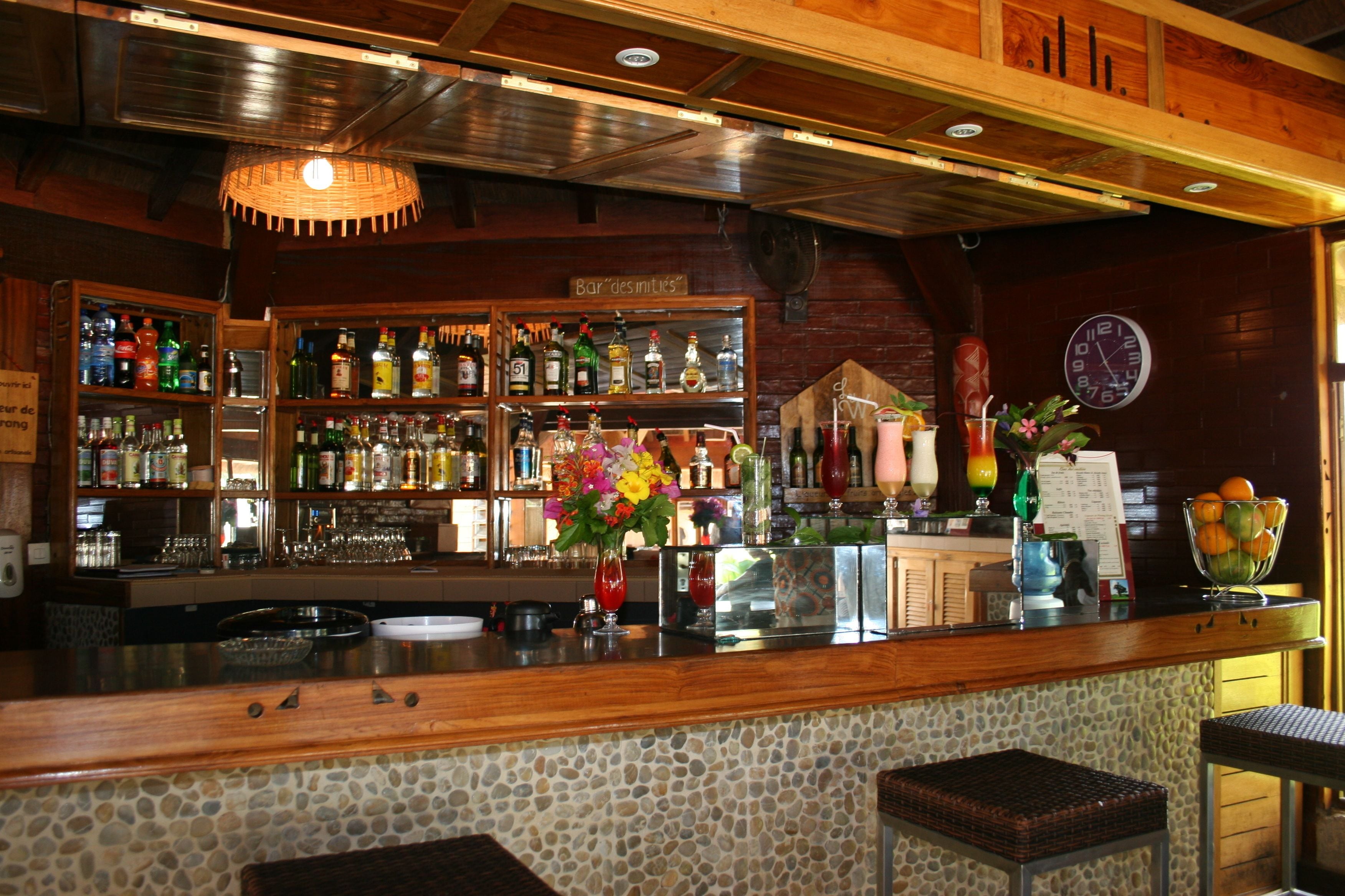 Una zona de bar con estantes llenos de botellas, un reloj y un jarrón de flores.