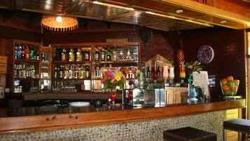 Una zona de bar con estantes llenos de botellas, un reloj y un jarrón de flores.