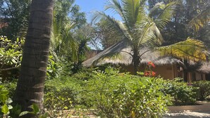 Um jardim tropical com palmeiras, uma cabana com telhado de palha e flores vibrantes.