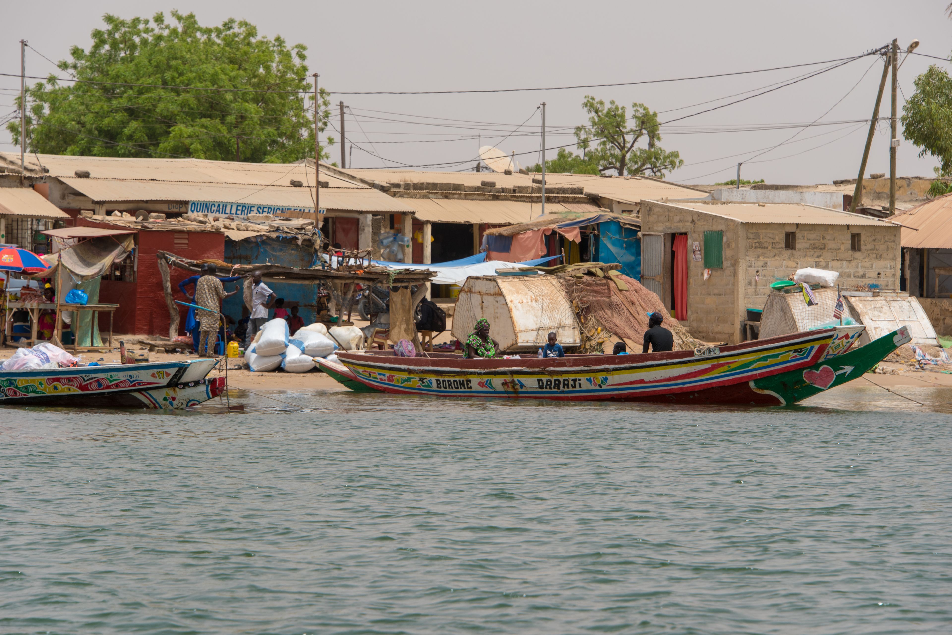 A boat with colorful decorations and text, docked near a building with a sign that reads "QUINCAILLERIE SERIE".