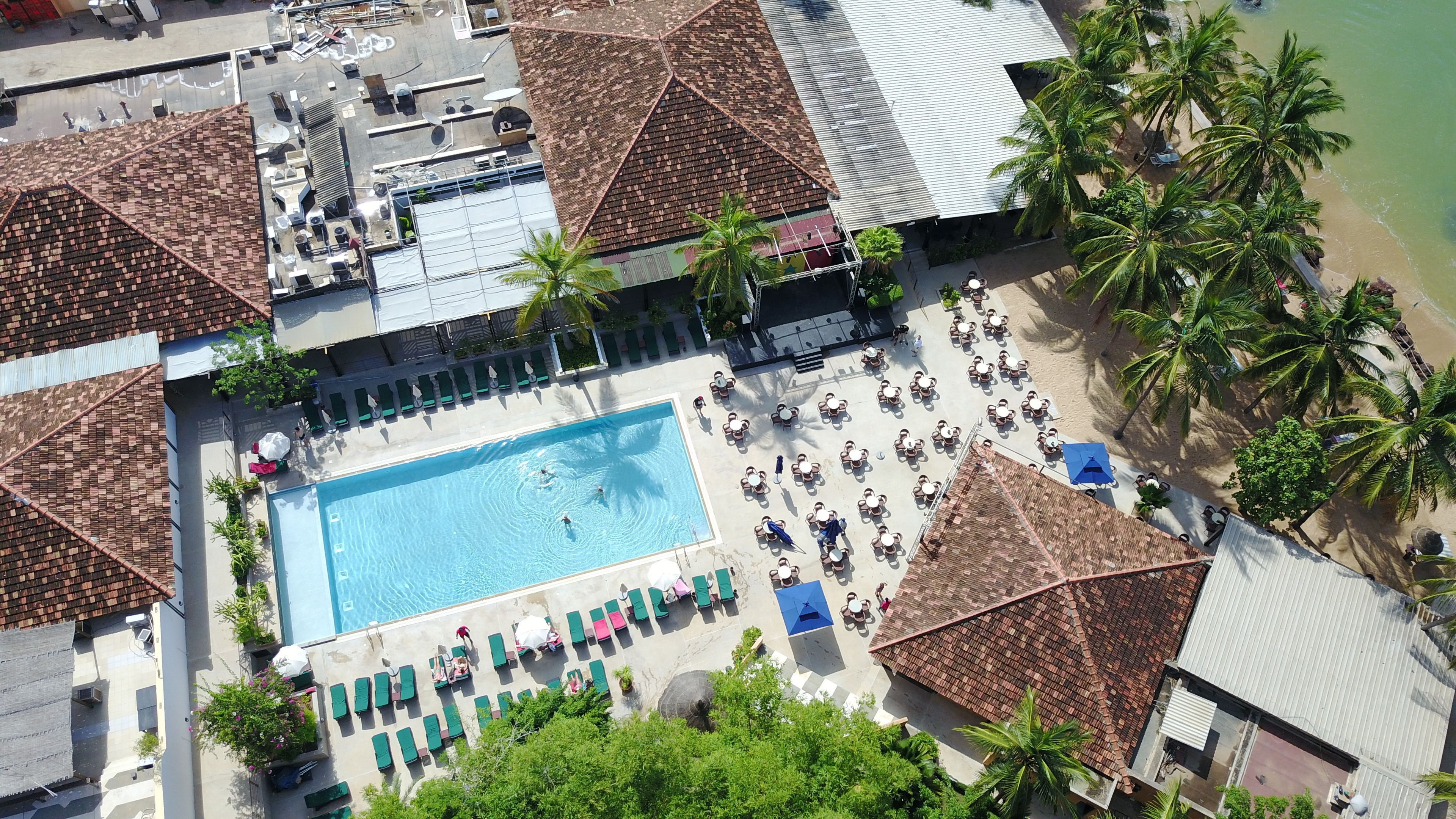 Vista aérea de um resort com piscina central, diversas áreas de descanso e palmeiras.