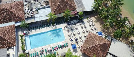 Vista aérea de um resort com piscina central, diversas áreas de descanso e palmeiras.