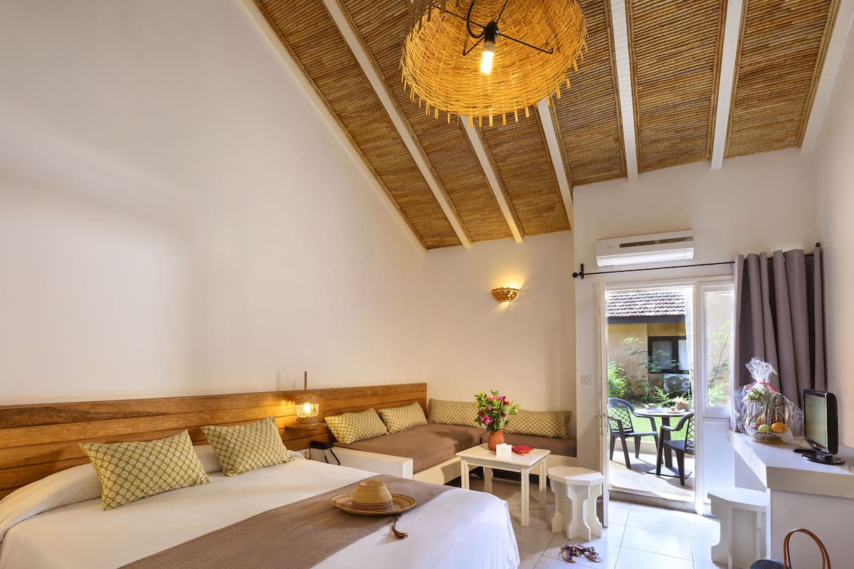 A bedroom with a large bed, a small table, and a wicker ceiling light.