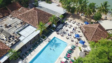 An aerial view of a resort with a swimming pool, lounge areas, and beach access.