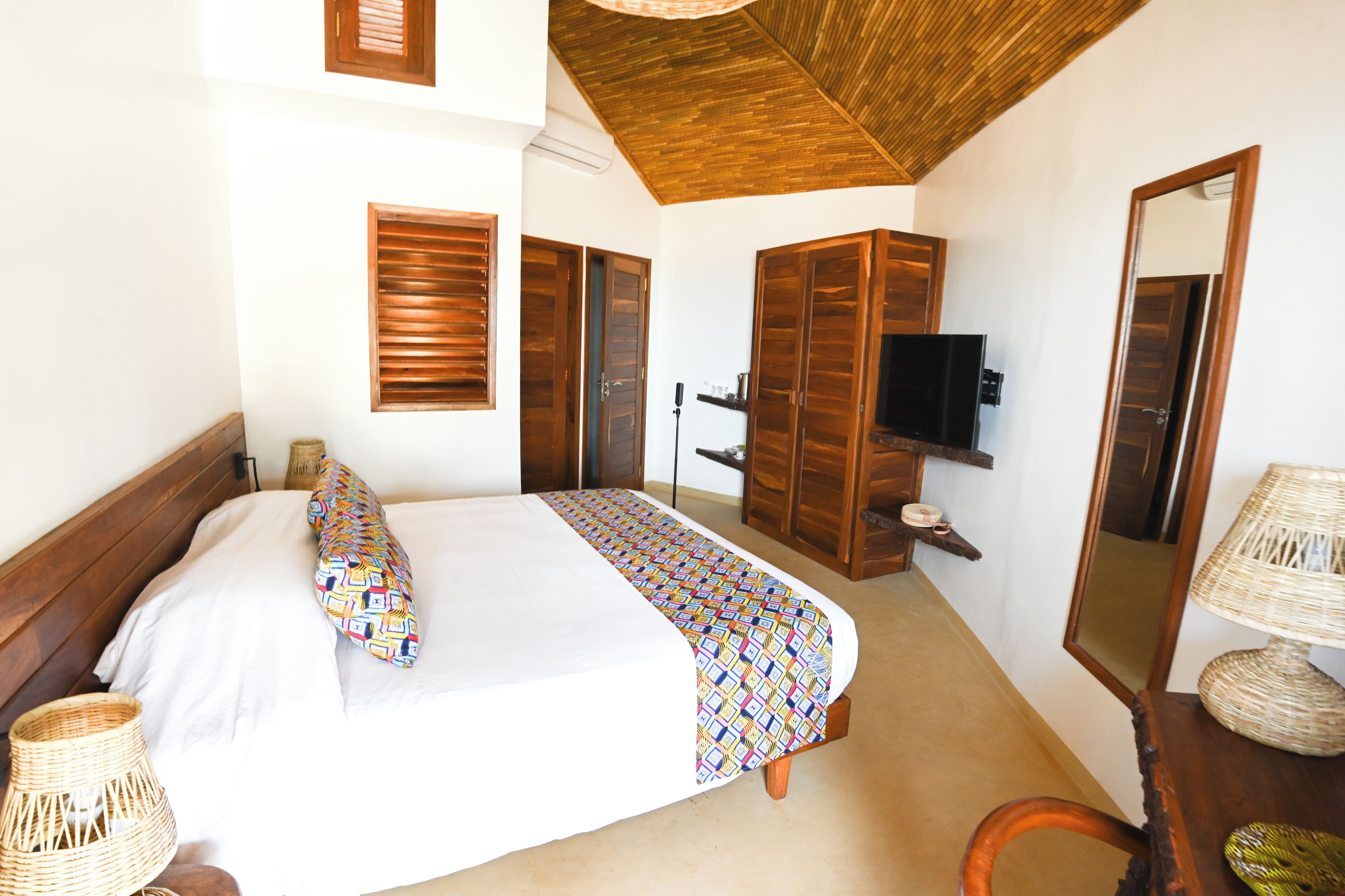 A bedroom with a bed, wooden wardrobe, television, and a mirror.