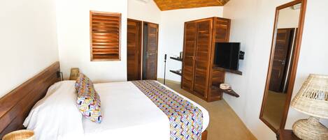 A bedroom with a bed, wooden wardrobe, television, and a mirror.