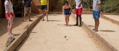 Un grupo de personas jugando al juego de bolos en un espacio al aire libre con suelo de arena y límites de madera.
