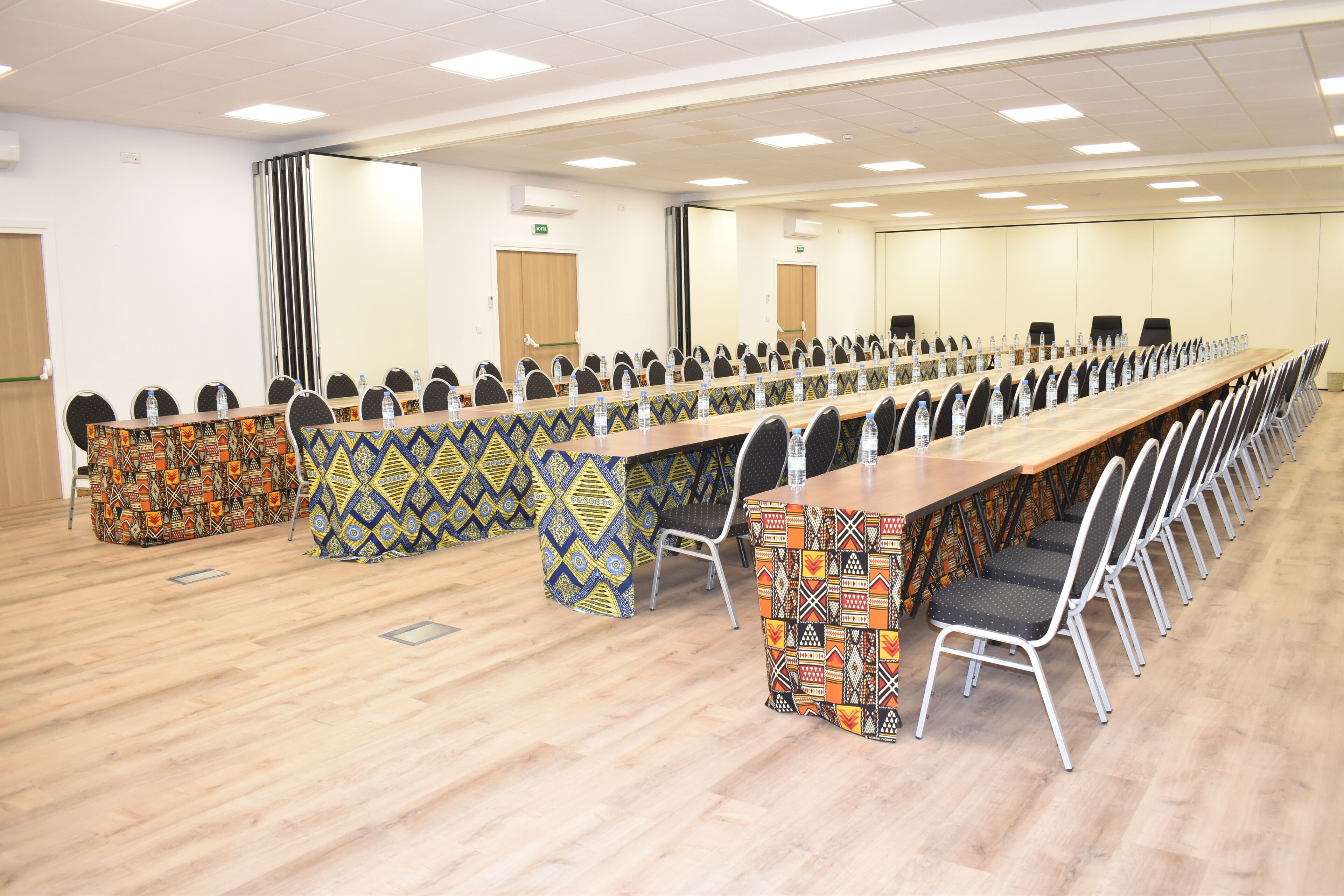 A conference room with long tables and chairs, equipped with water bottles and a patterned tablecloth.