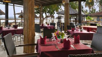 An outdoor restaurant with tables set for dining, featuring wicker chairs and red tablecloths.