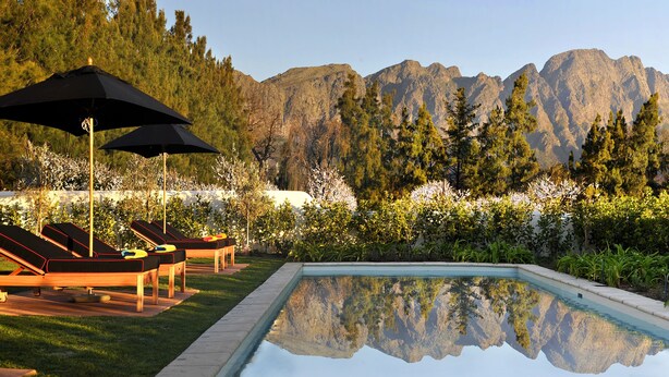 A pool with a mountain backdrop, lounge chairs, and umbrellas. - La Clé Village (Franschhoek)