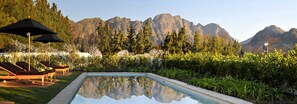 A pool with a mountain backdrop, lounge chairs, and umbrellas. - La Clé Village (Franschhoek)