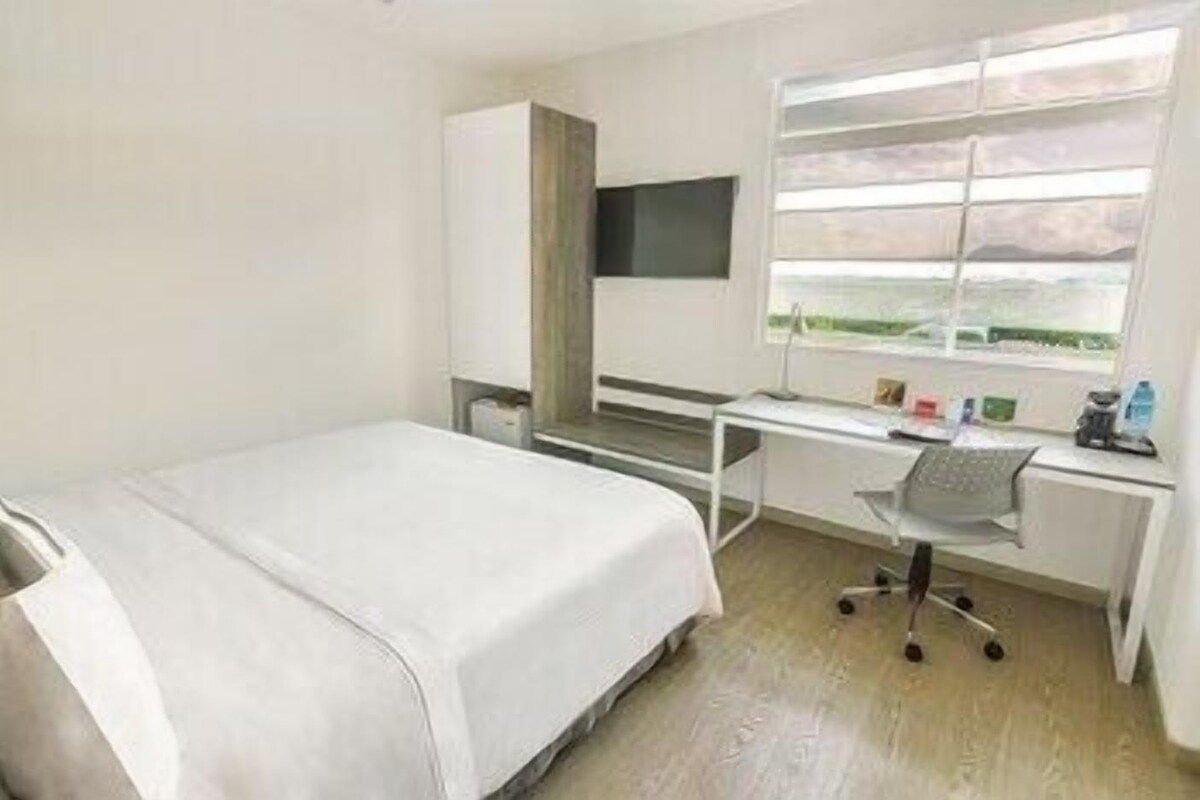 Una habitación con una cama, un escritorio, una silla y una ventana con persianas.