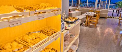 Un bufé con diversos productos de panadería y una zona de estar con mesas y sillas.