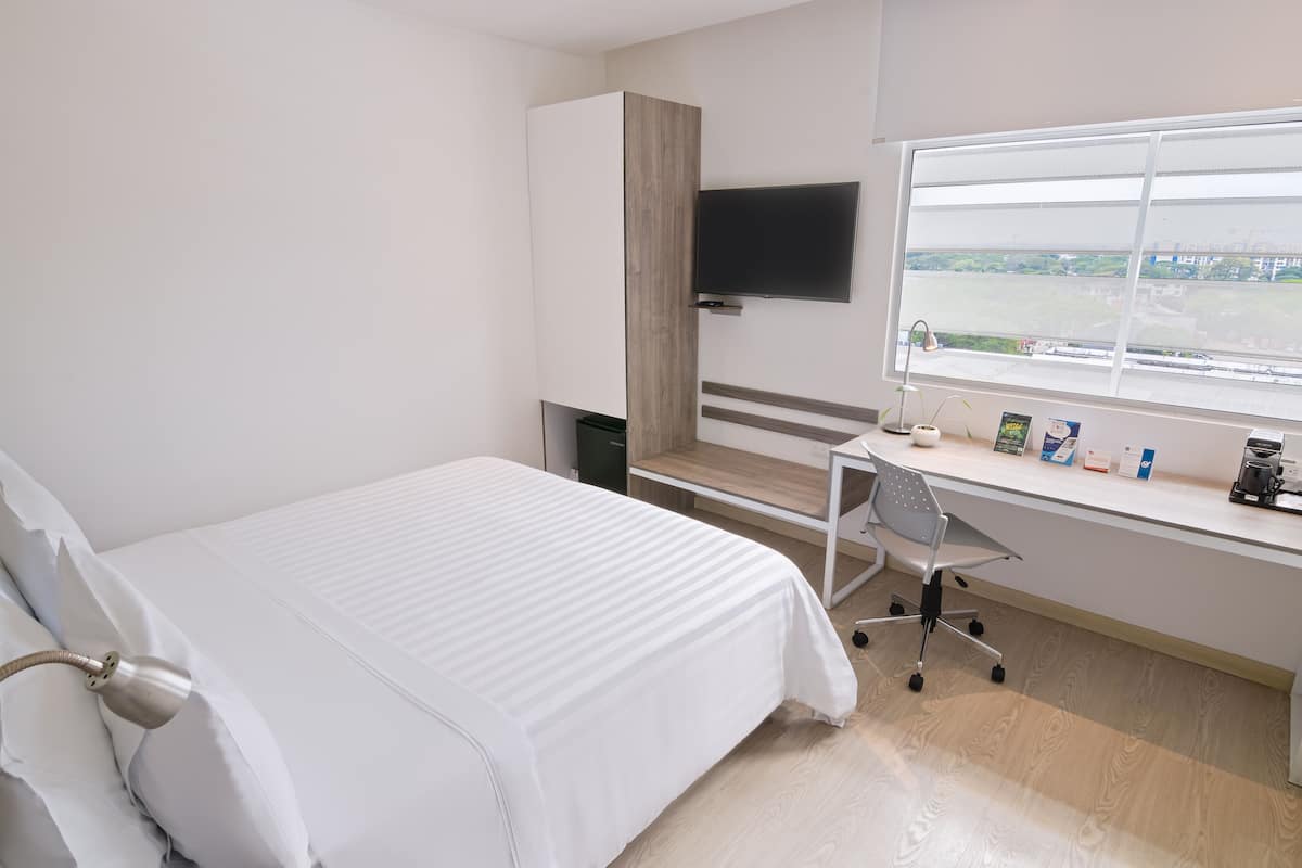 Habitación de hotel con cama, escritorio, silla, televisor y ventana con vistas a un campo.