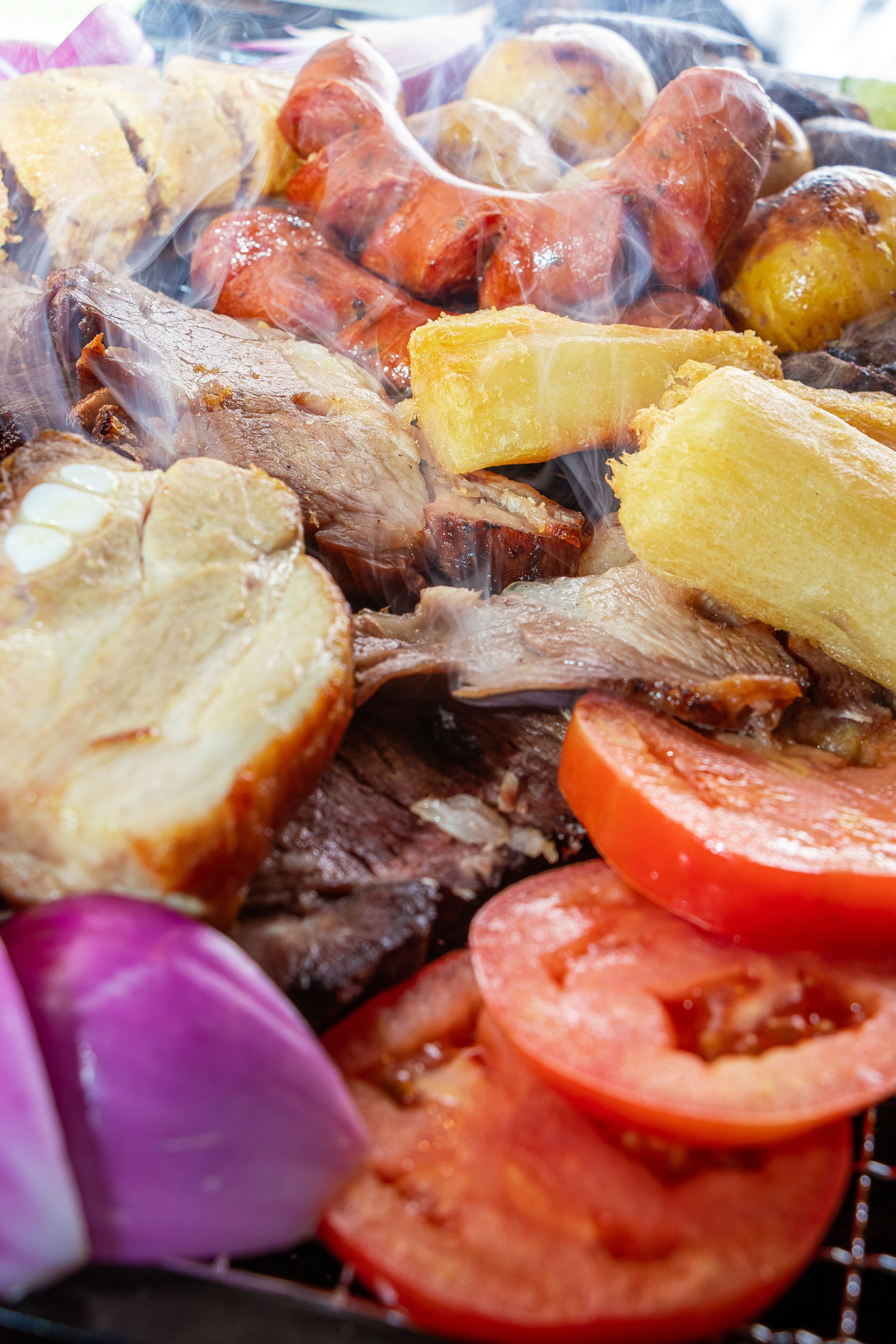 Primer plano de una variedad de carnes y verduras a la parrilla, incluyendo salchichas, papas y tomates.