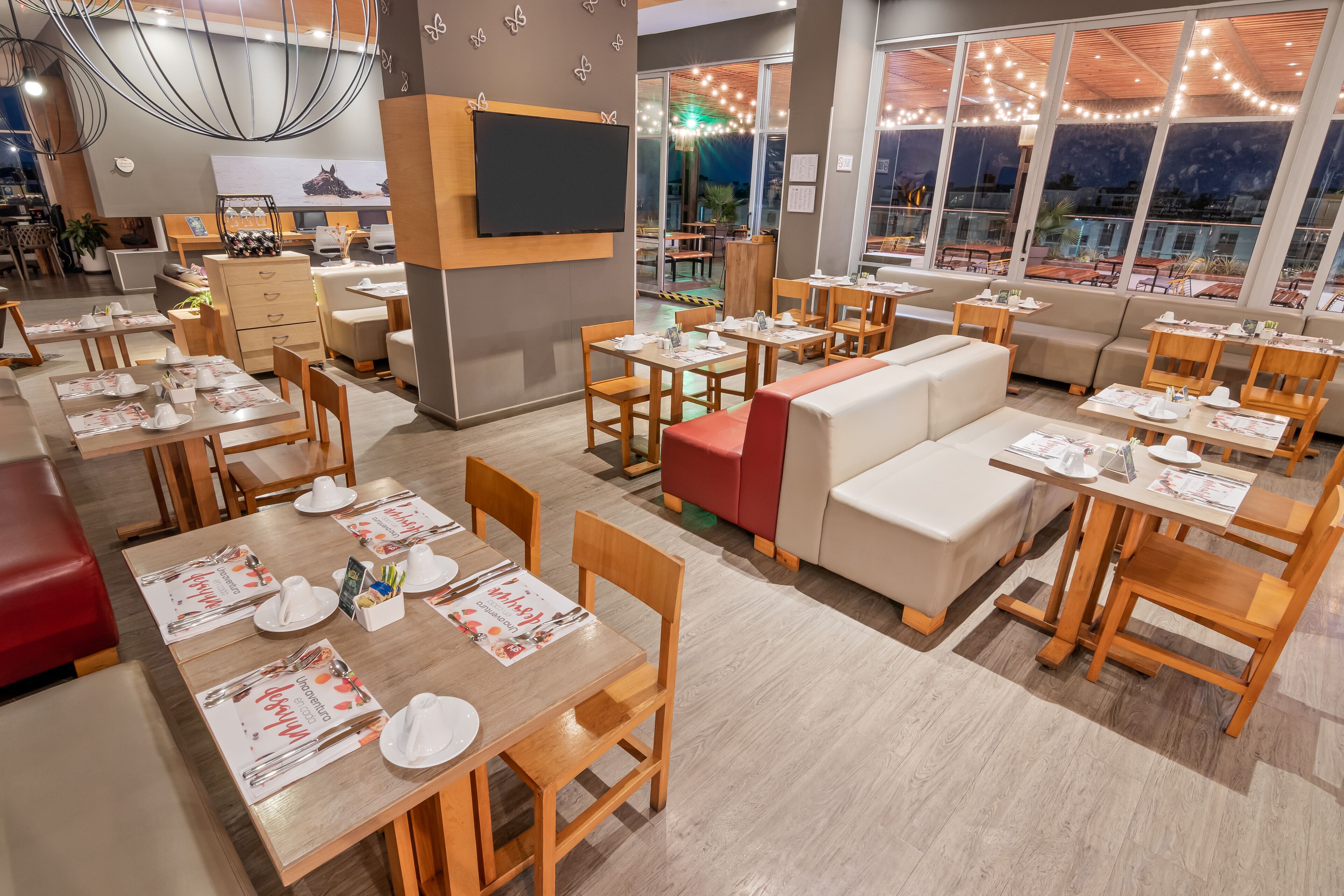 Un restaurant doté de plusieurs espaces de restauration, notamment des banquettes et des tables, où les menus et les couverts sont disposés.