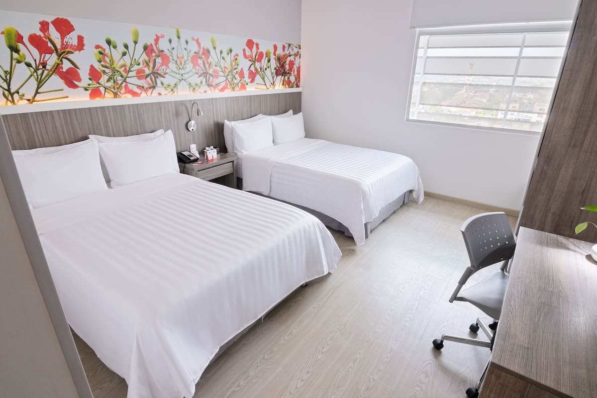 Habitación de hotel con dos camas, un escritorio, una silla y una ventana con vistas.