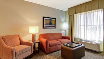 Ein Hotelzimmer mit Ohrensessel, Sofa, kleinem Tisch, Lampe, Heizkörper und einem Fenster mit Vorhängen.