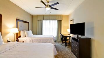 Ein Hotelzimmer mit zwei Betten, einem Schreibtisch, einem Fernseher und einem Deckenventilator.