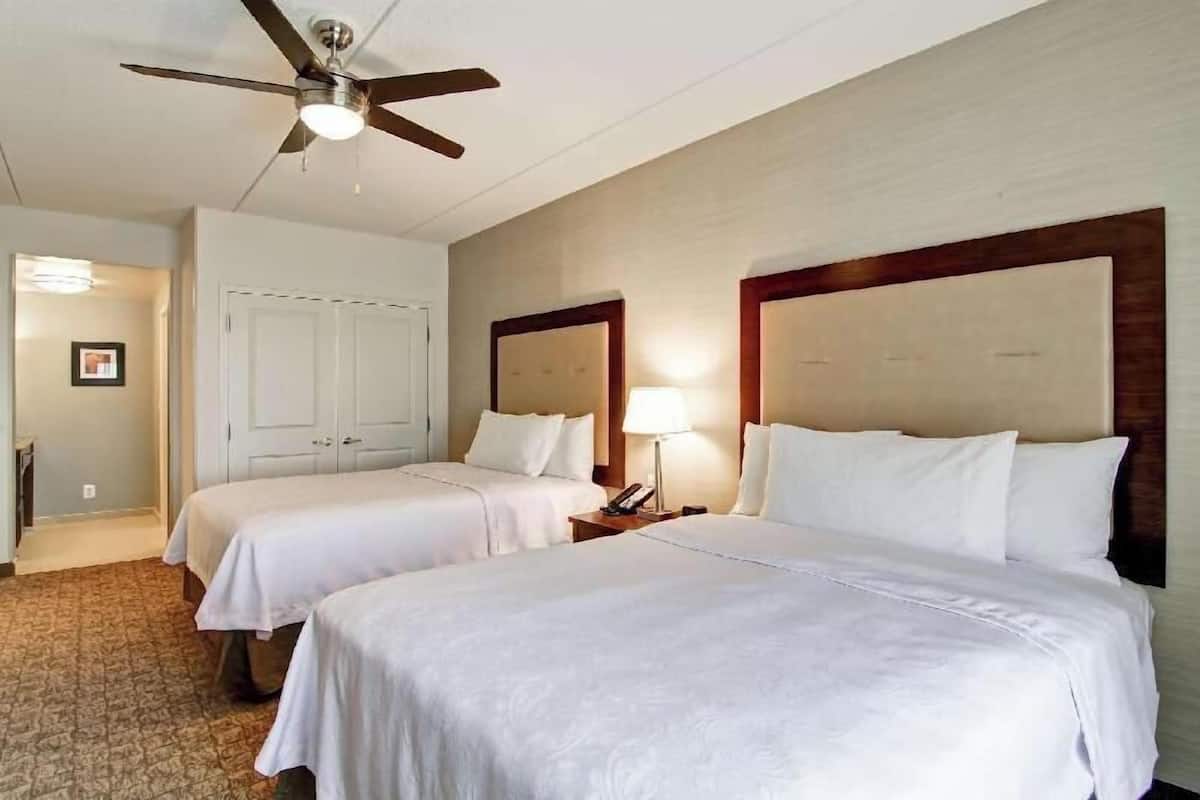 Une chambre d’hôtel avec deux lits, un ventilateur de plafond, une lampe de chevet et une porte donnant sur une autre pièce.