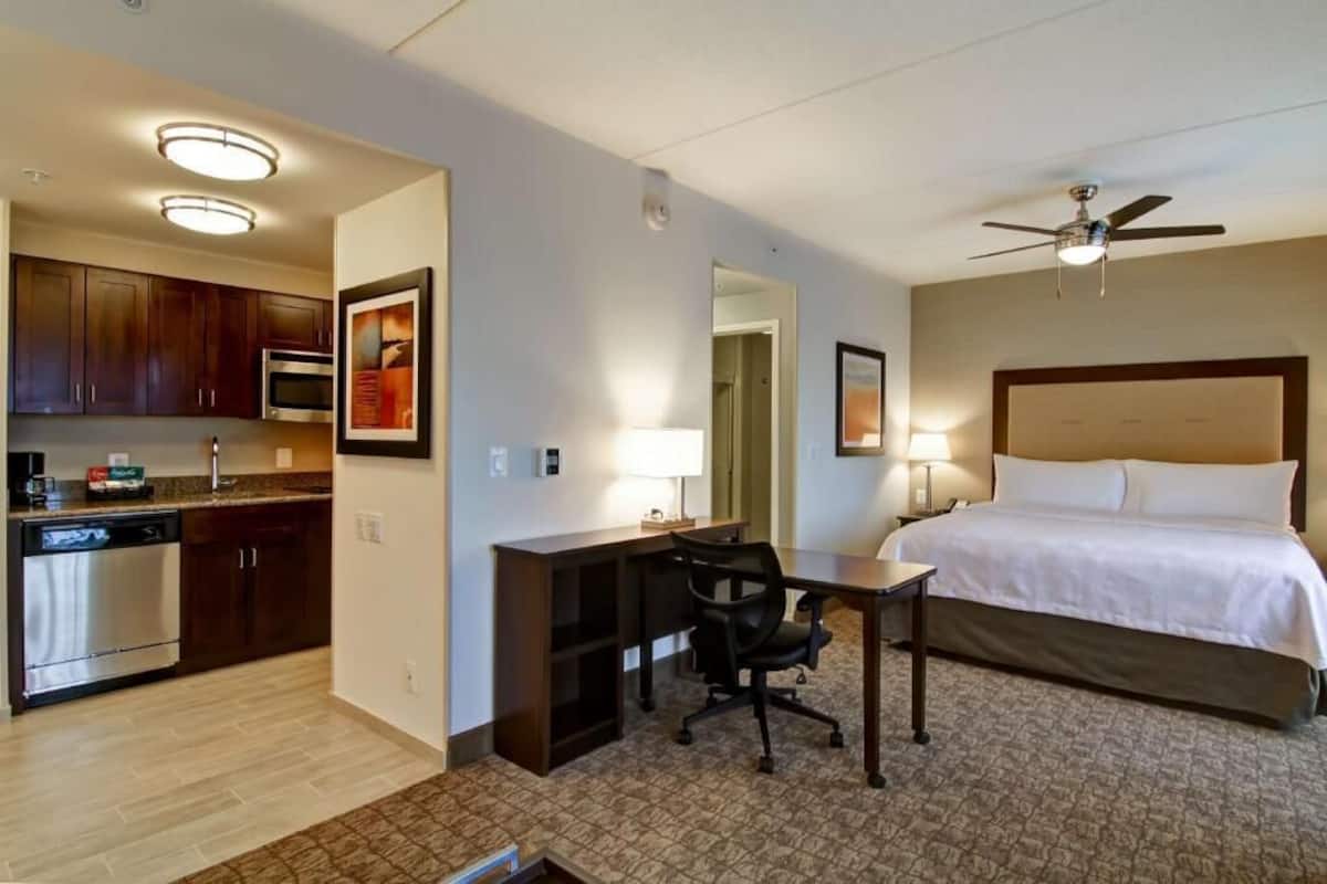 Une chambre d’hôtel équipée d’un lit, d’un bureau, d’une chaise, d’une kitchenette et d’un ventilateur de plafond.