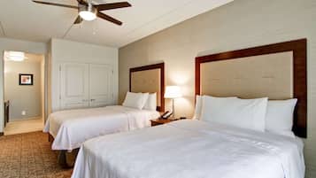 Habitación de hotel con dos camas, un ventilador de techo, una mesita de noche con lámpara y una puerta que da a otra habitación.