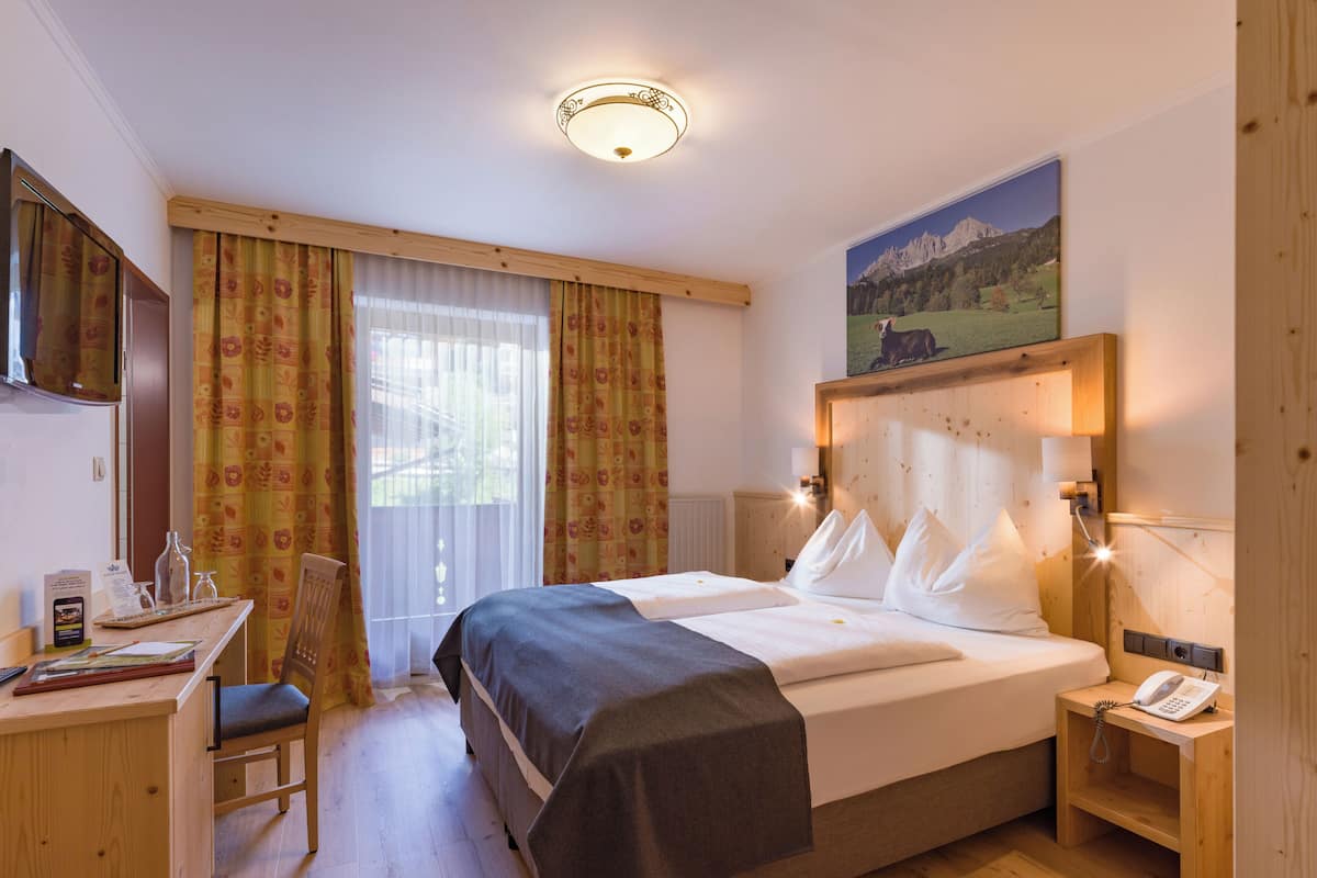 A hotel room with a wooden bed, a desk, a chair, a television, and a painting on the wall.