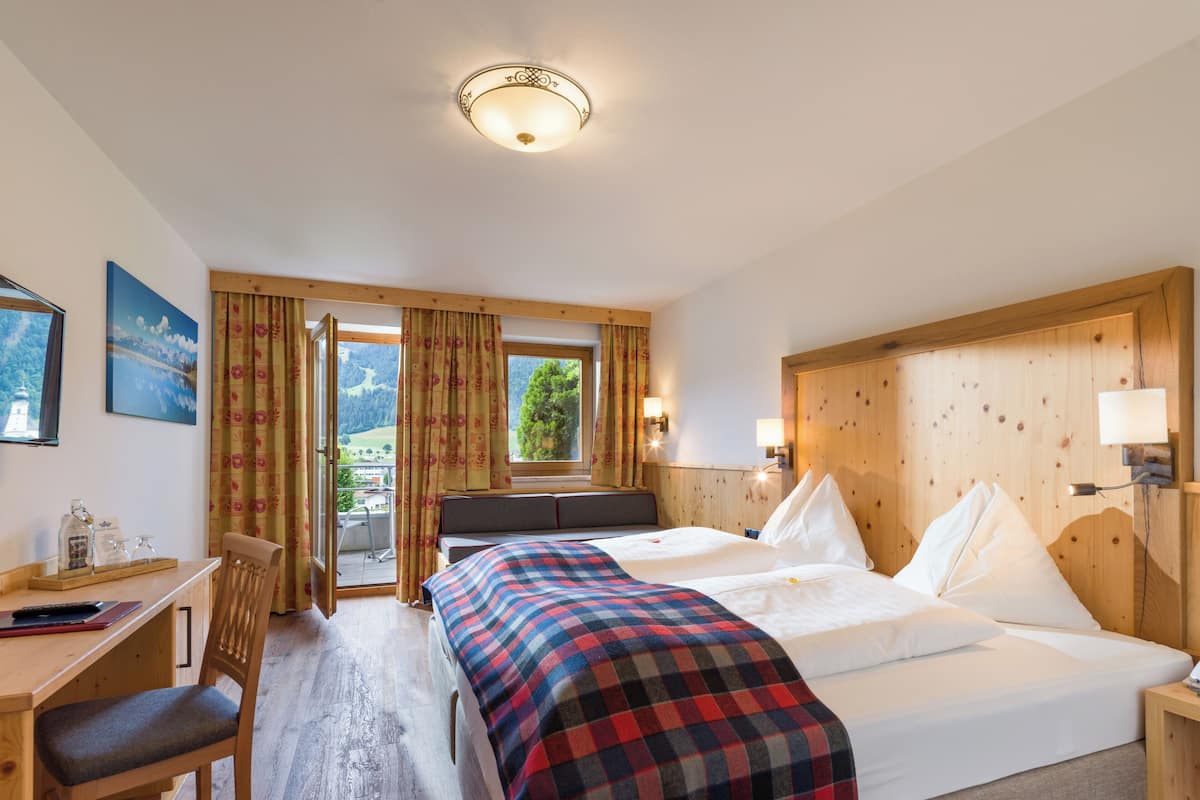 A hotel room with a bed, desk, chair, and a view of the outdoors.