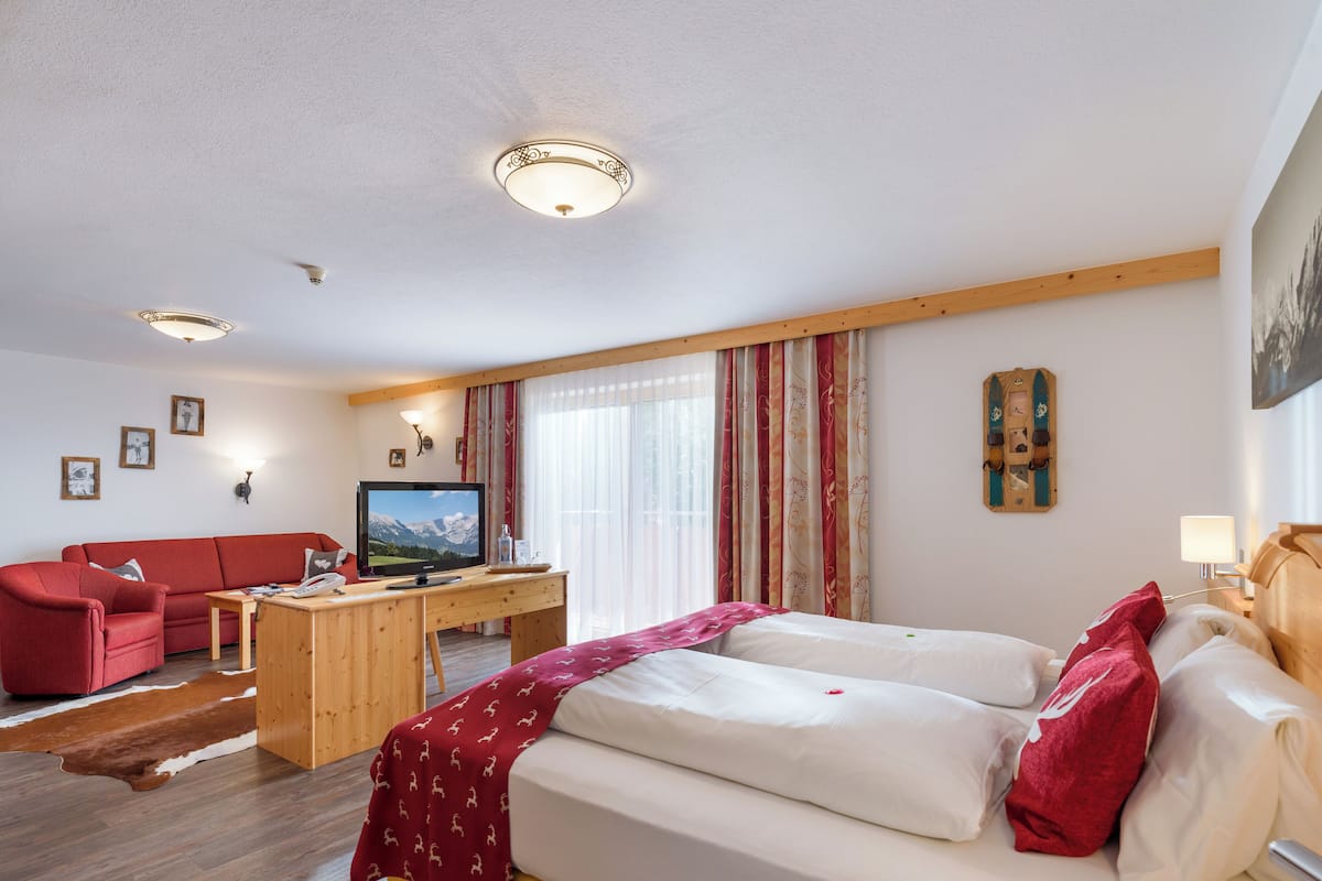 A hotel room with a bed, a desk with a TV, a sofa, and a window with curtains.