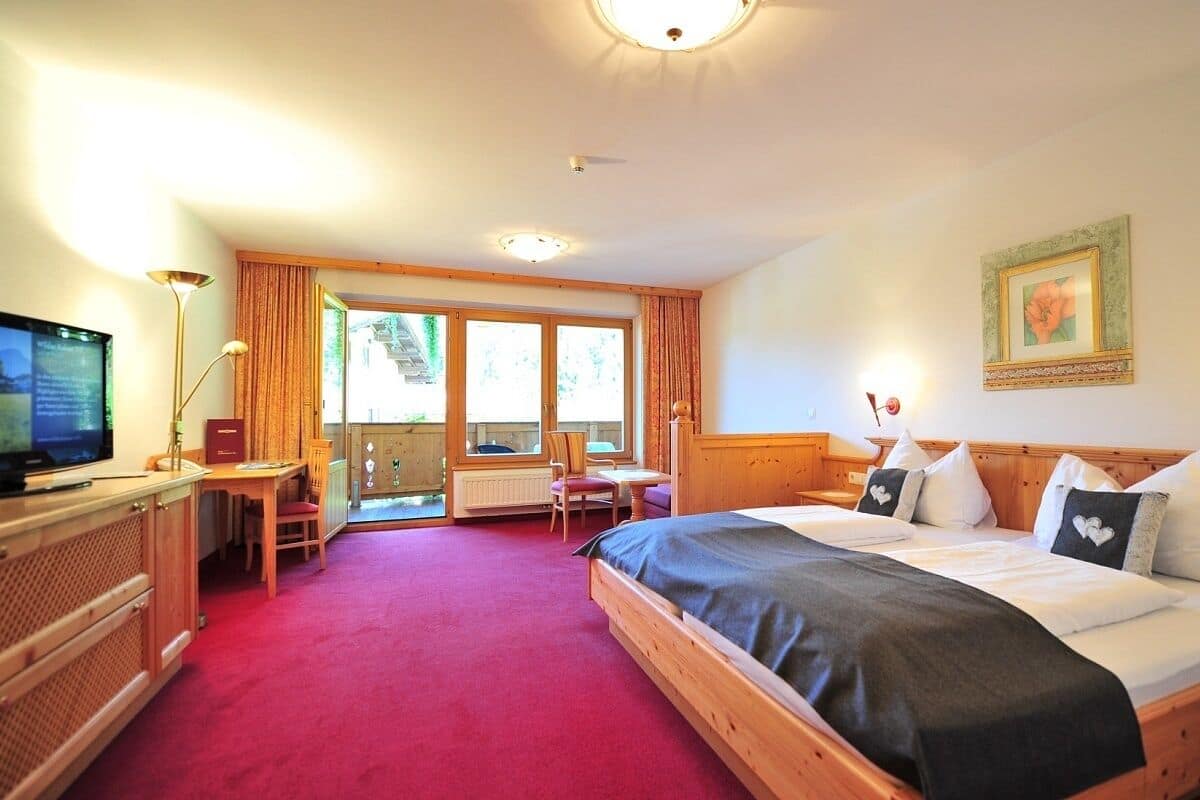 A hotel room with a large bed, a desk with a chair, a television, and a window with curtains.