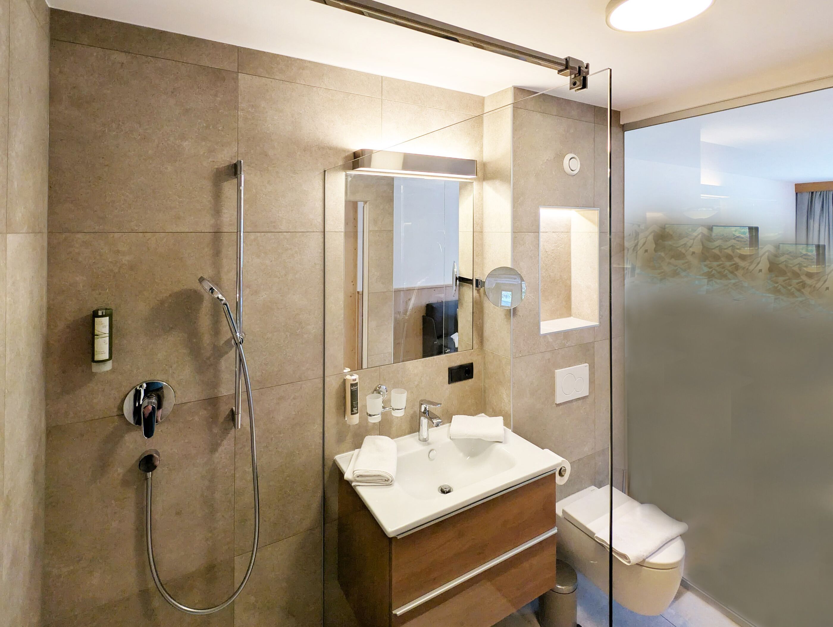 Une salle de bain moderne avec une douche à l’italienne en verre, un grand miroir, un lavabo avec un meuble-vasque et des toilettes.