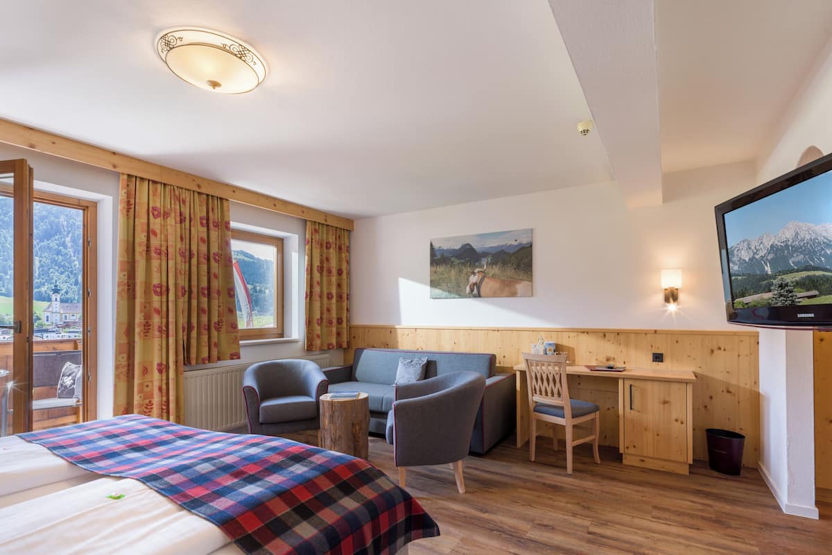A hotel room with a bed, a desk, a chair, a TV, and a view of mountains.